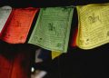 A close-up of colorful Tibetan prayer flags hanging indoors, featuring intricate designs and text.