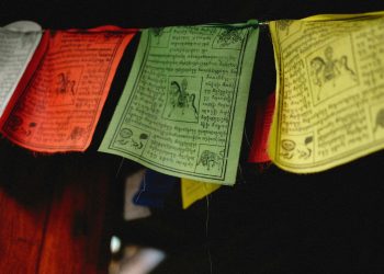 A close-up of colorful Tibetan prayer flags hanging indoors, featuring intricate designs and text.