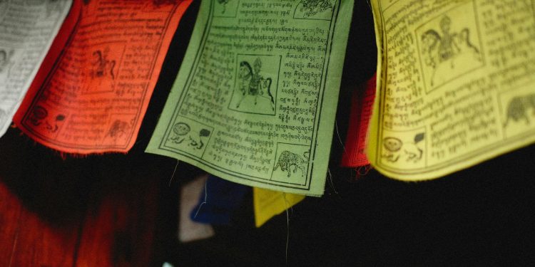 A close-up of colorful Tibetan prayer flags hanging indoors, featuring intricate designs and text.