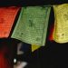 A close-up of colorful Tibetan prayer flags hanging indoors, featuring intricate designs and text.