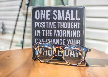 Eyeglasses resting on a table in front of a motivational quote sign, emphasizing positivity.