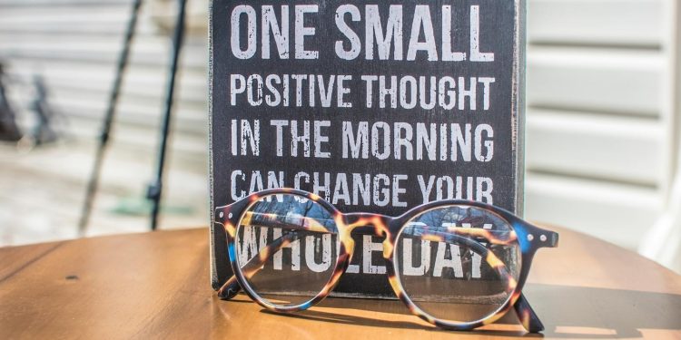 Eyeglasses resting on a table in front of a motivational quote sign, emphasizing positivity.