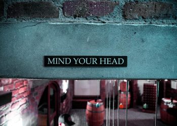 A 'Mind Your Head' sign in a rustic brick barrel cellar setting, creating a safety awareness ambiance.