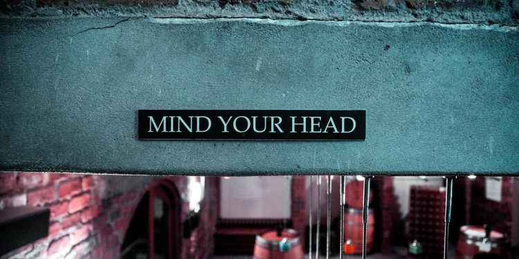 A 'Mind Your Head' sign in a rustic brick barrel cellar setting, creating a safety awareness ambiance.
