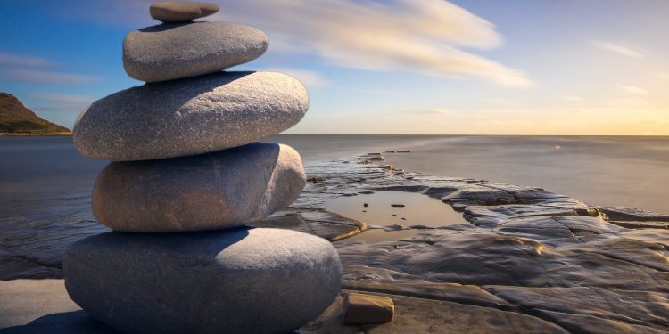 A serene stack of stones on the rocky seashore during a peaceful sunrise, embodying balance and zen.