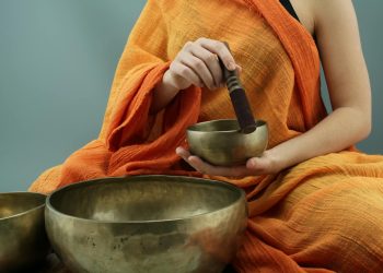Person in traditional attire using Tibetan singing bowls in a meditative practice.