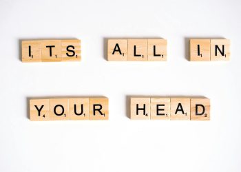 Wooden Scrabble tiles arranged to spell 'ITS ALL IN YOUR HEAD' on a white background.