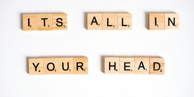 Wooden Scrabble tiles arranged to spell 'ITS ALL IN YOUR HEAD' on a white background.
