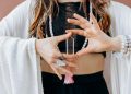 A woman wearing jewelry holds a clear healing crystal, symbolizing spiritual wellness.