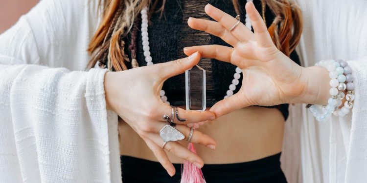 A woman wearing jewelry holds a clear healing crystal, symbolizing spiritual wellness.