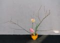 A serene minimalist floral arrangement in a wooden vase with branches and blooms.