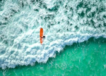 Surfer on orange board rides turquoise wave
