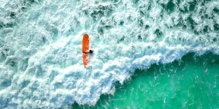 Surfer on orange board rides turquoise wave