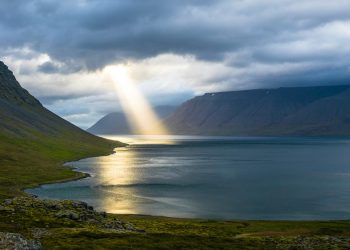 sun reflection on calm water near green mountains