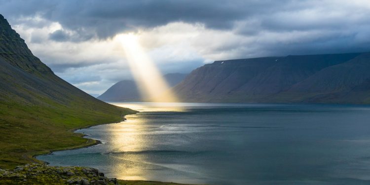 sun reflection on calm water near green mountains