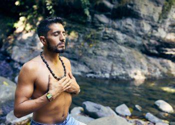 topless man wearing black beaded necklace and blue denim shorts standing on rocky shore during daytime