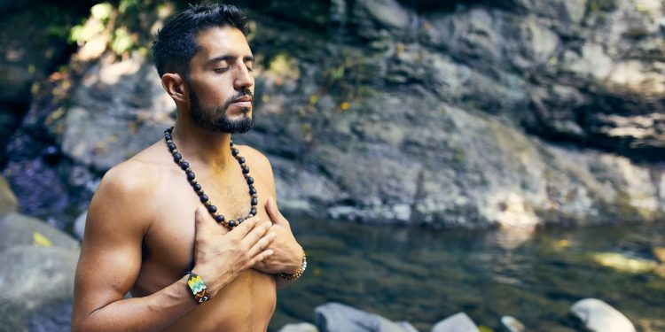 topless man wearing black beaded necklace and blue denim shorts standing on rocky shore during daytime