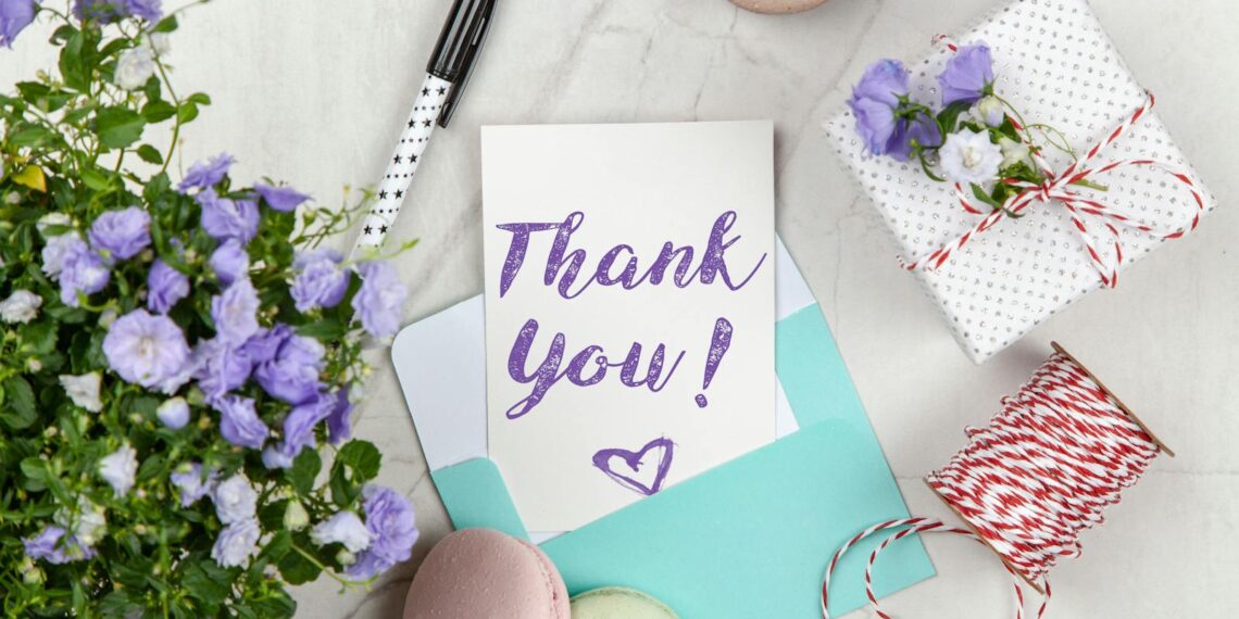 A beautifully arranged thank you card with lavender flowers, macarons, and gift package on a marble desk.