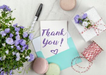 A beautifully arranged thank you card with lavender flowers, macarons, and gift package on a marble desk.