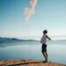 man standing on sand while spreading arms beside calm body of water