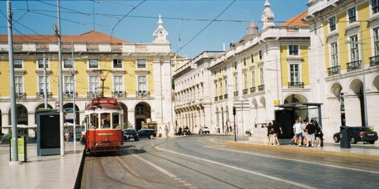 A red tram travels down a street in lisbon.