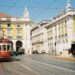 A red tram travels down a street in lisbon.