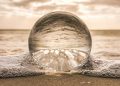 A crystal ball resting on Bonita Springs beach reflecting ocean waves at sunset.