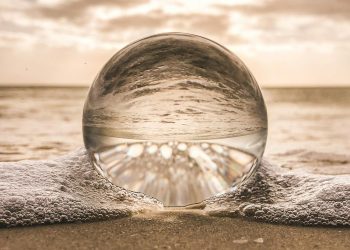 A crystal ball resting on Bonita Springs beach reflecting ocean waves at sunset.