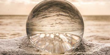 A crystal ball resting on Bonita Springs beach reflecting ocean waves at sunset.