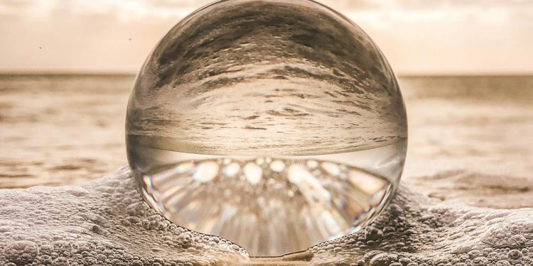 A crystal ball resting on Bonita Springs beach reflecting ocean waves at sunset.