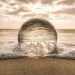 A crystal ball resting on Bonita Springs beach reflecting ocean waves at sunset.